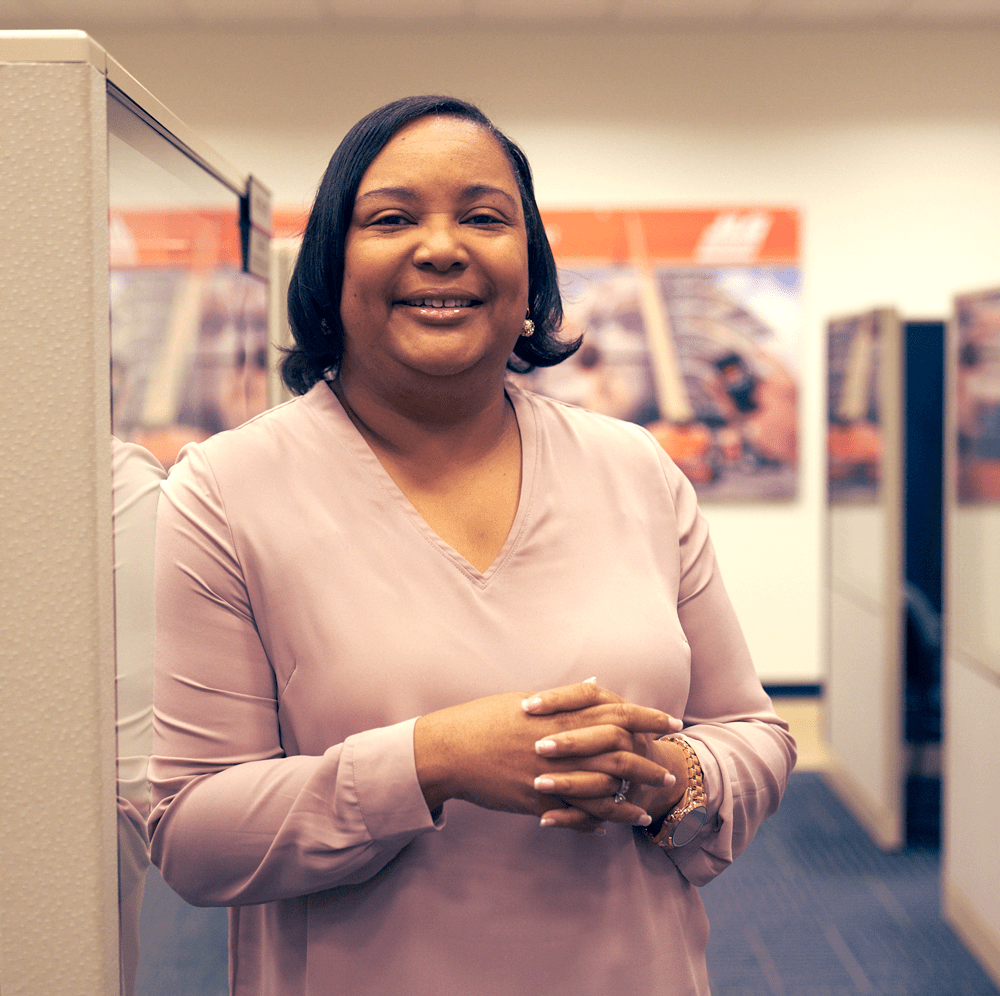 Black female wearing a pink shirt standing inside an office building smiling