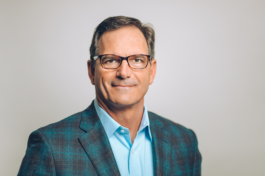 Head shot of CEO, Wilson Jones, in a blue shirt and checker patterned jacket wearing glasses
