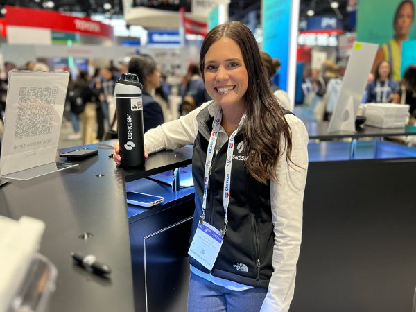 Young female with brown hair wearing a black vest and white long sleeve shirt standing at a table