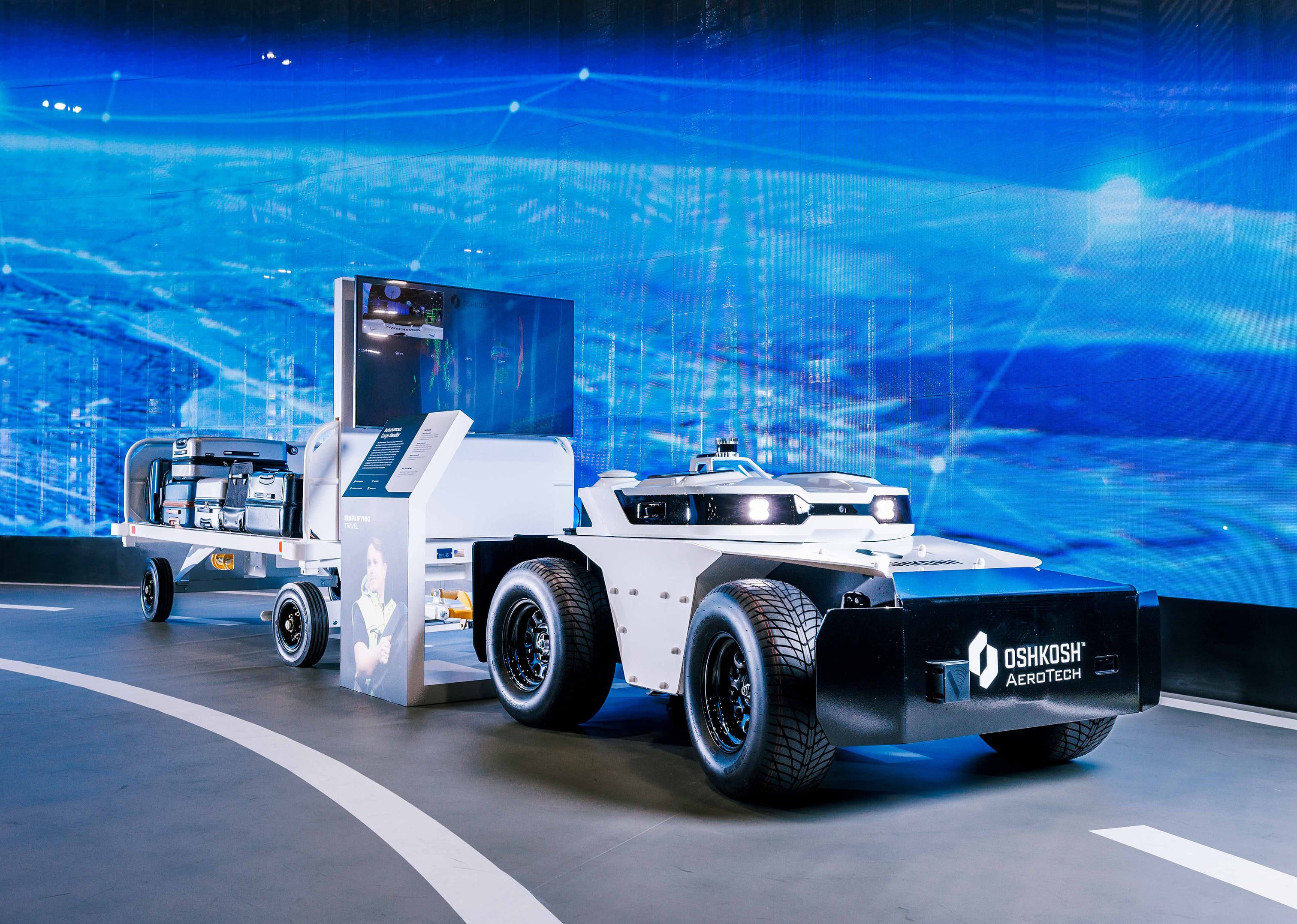 Oshkosh AeroTech cargo-handling vehicle designed for airport operations, showcased against a futuristic digital backdrop at CES.