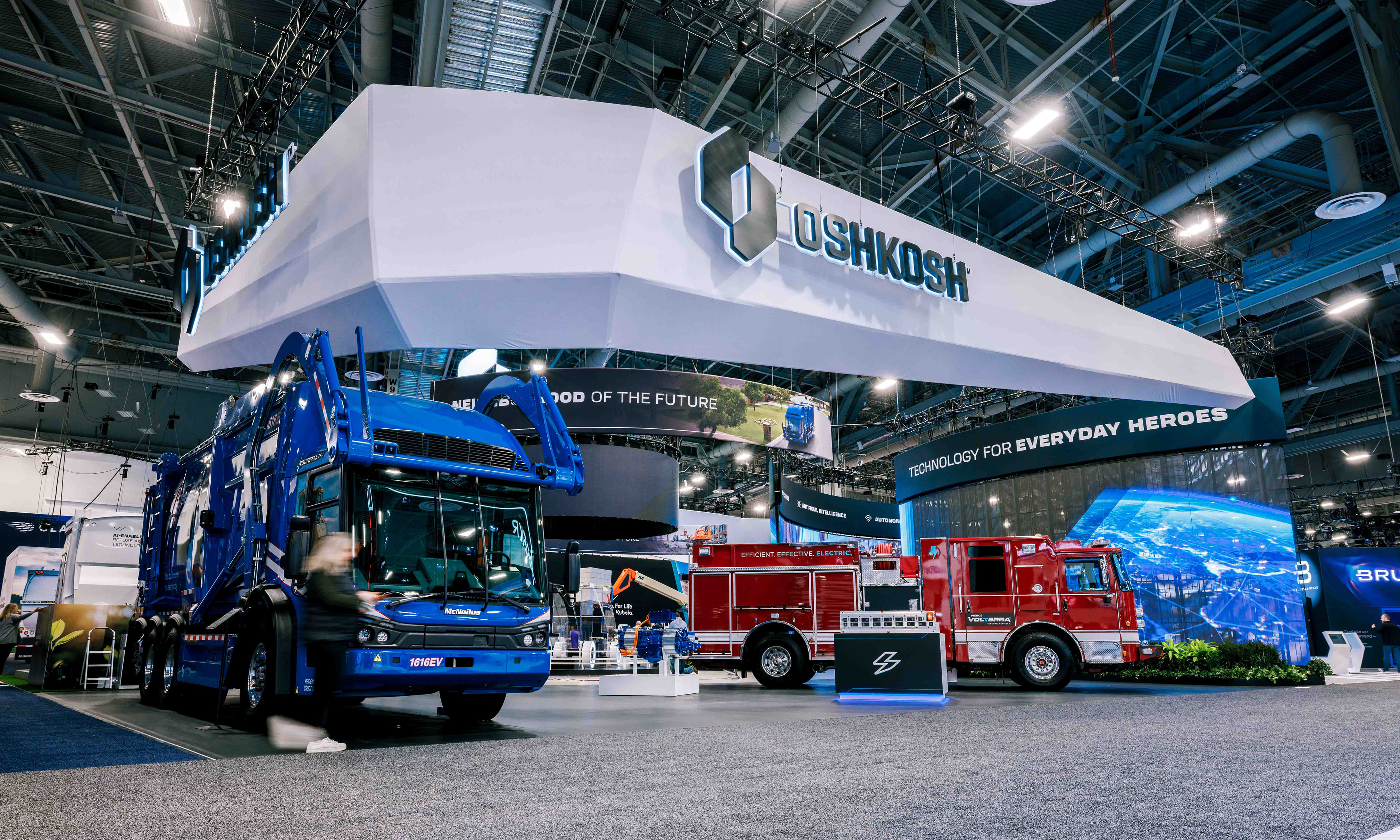 A bustling view of the Oshkosh Corporation booth at CES, displaying various heavy-duty vehicles and innovations.
