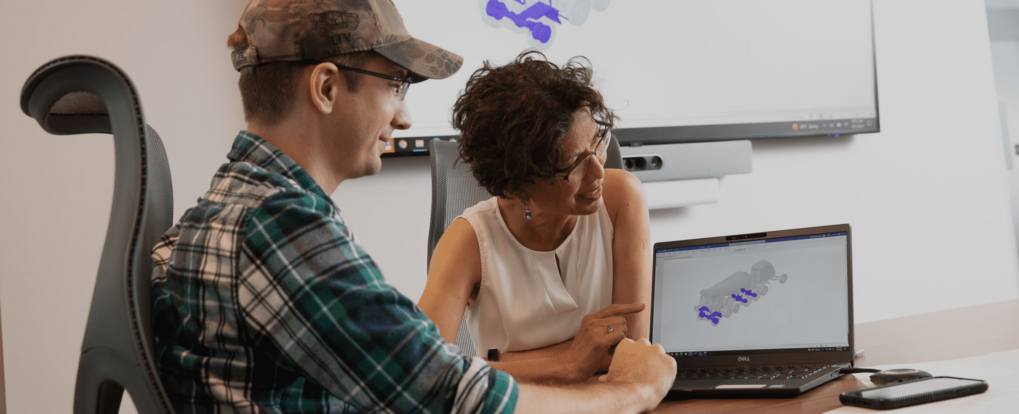 Female and male engineer looking at a computer with a truck schematic showing and tv in the background