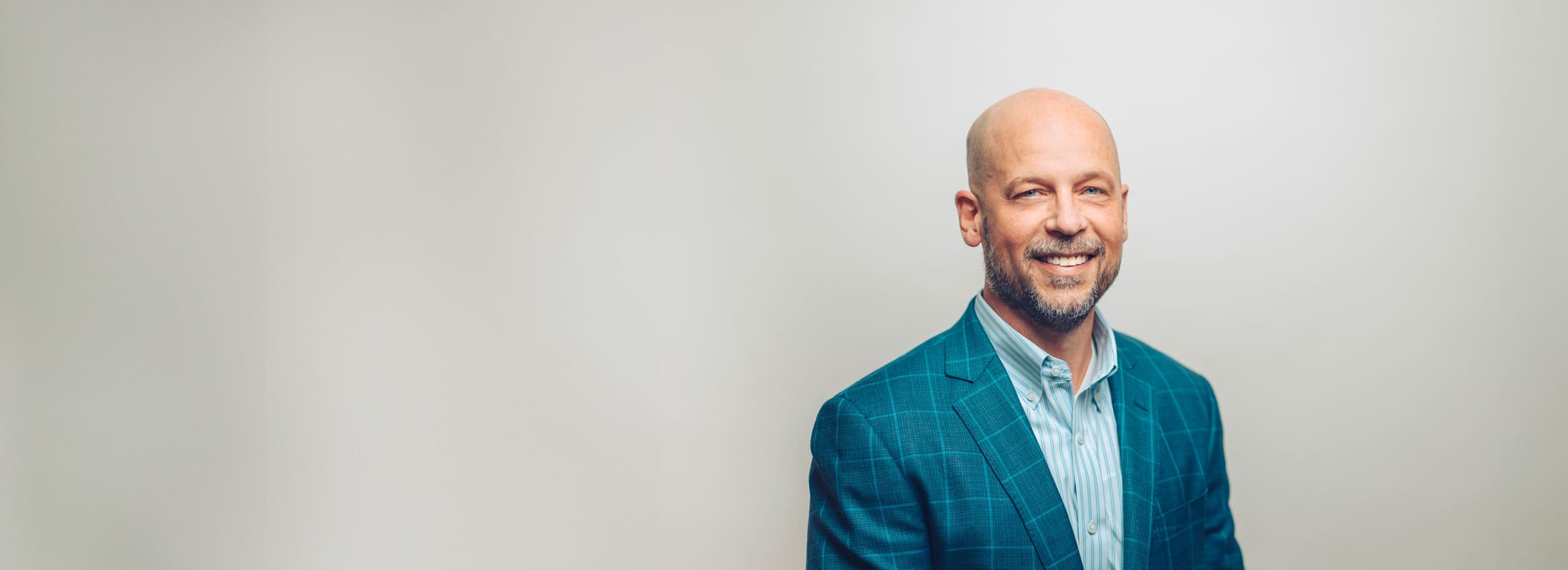Oshkosh CEO, John Pfeifer, wearing a blue suit coat and blue striped button up shirt