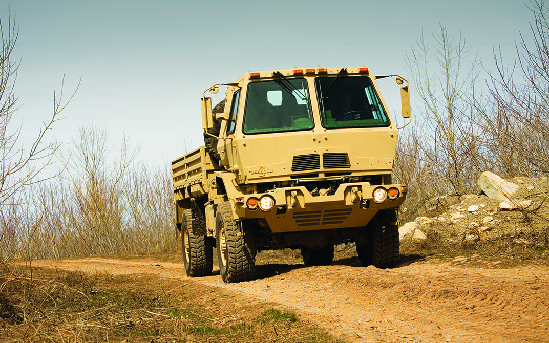 Cream Oshkosh FMTV driving on a dirt road