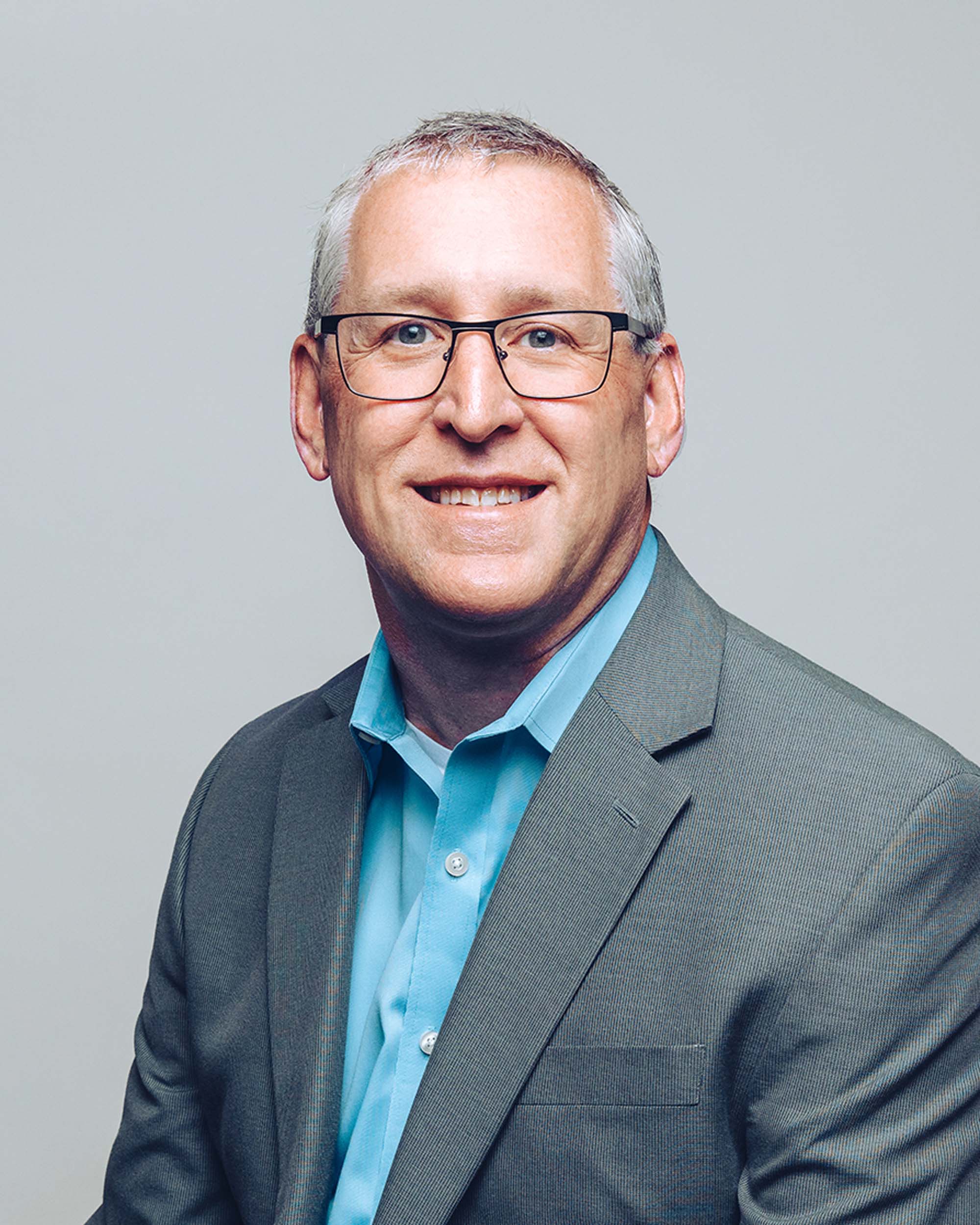 Chris Freeders smiling and wearing a grey suit jacket on top of a light blue shirt