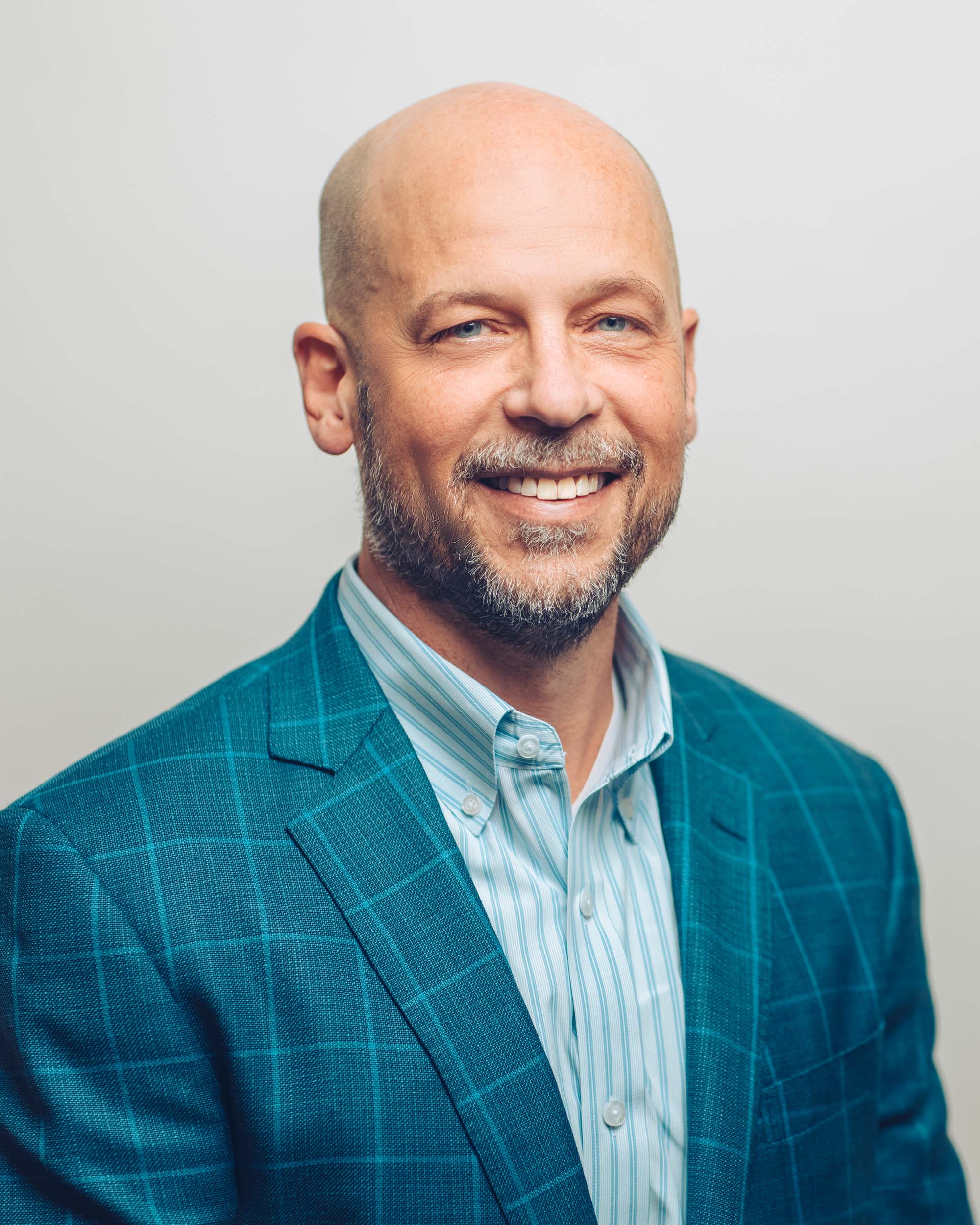 John Pfeifer wearing a blue patterned suit coat smiling