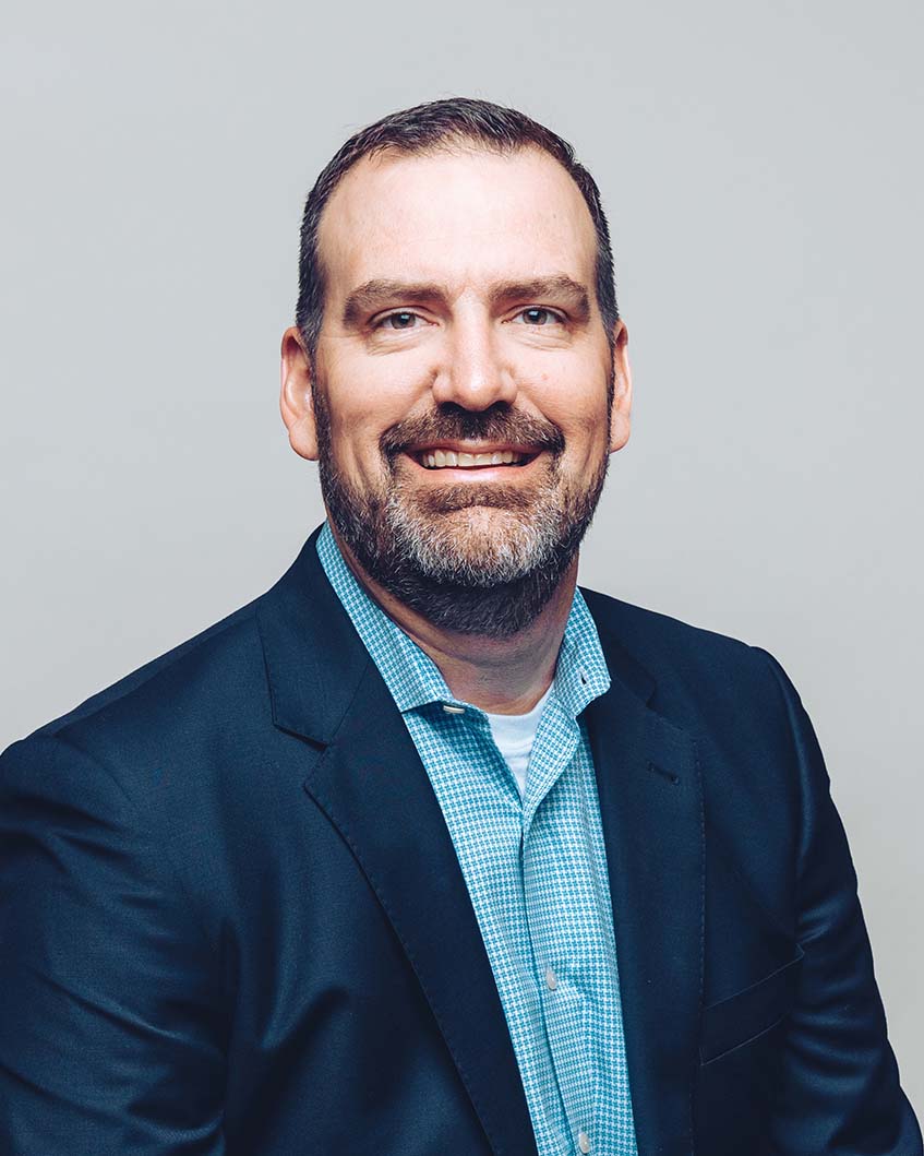 Mike Pack smiling and wearing a dark navy suit jacket