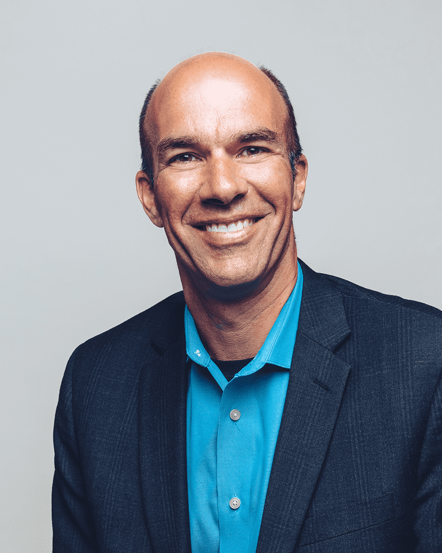 Professional photo of Tim Bleck in a navy jacket and teal blue button up shirt with a grey background