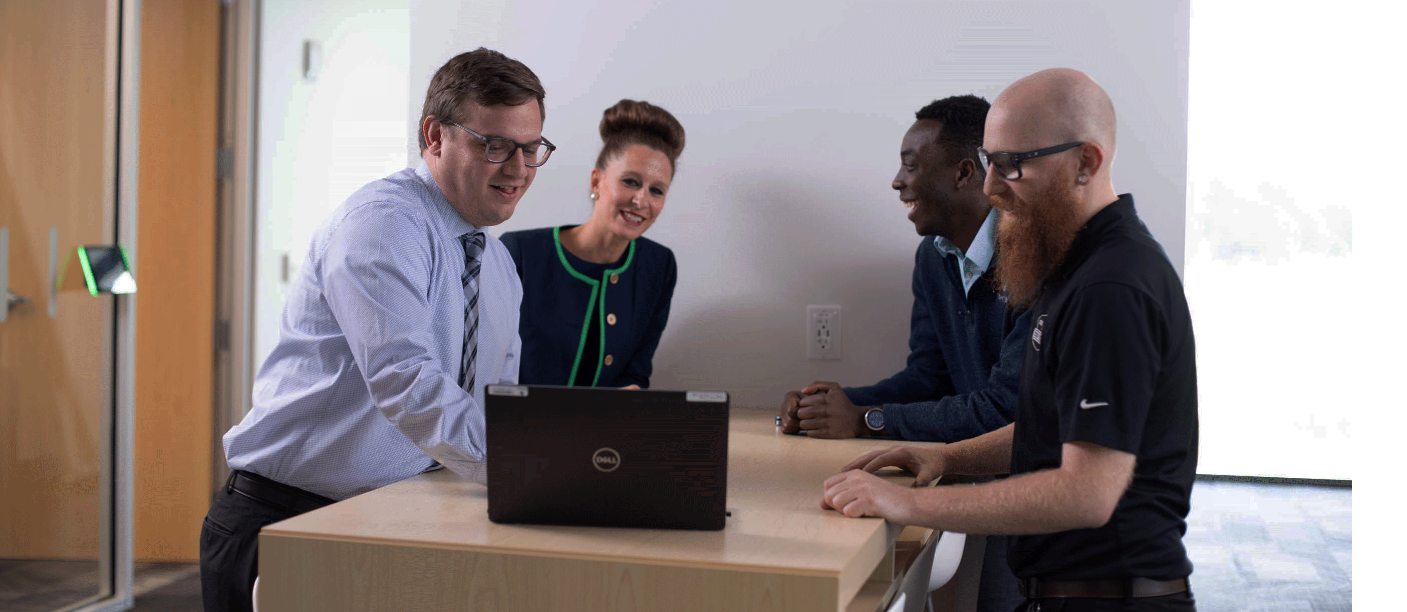 Three males and one female team members collaborating at a high top desk in an office with a laptop in front of them