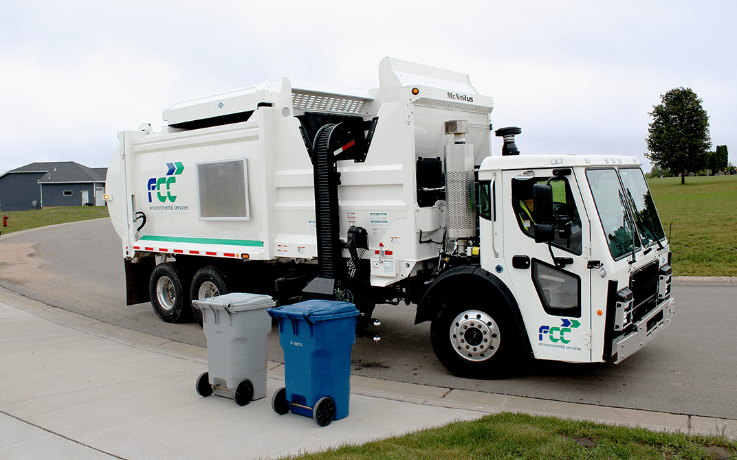 White zero radius side loader refuse collection vehicle in a neighborhood picking up garbage