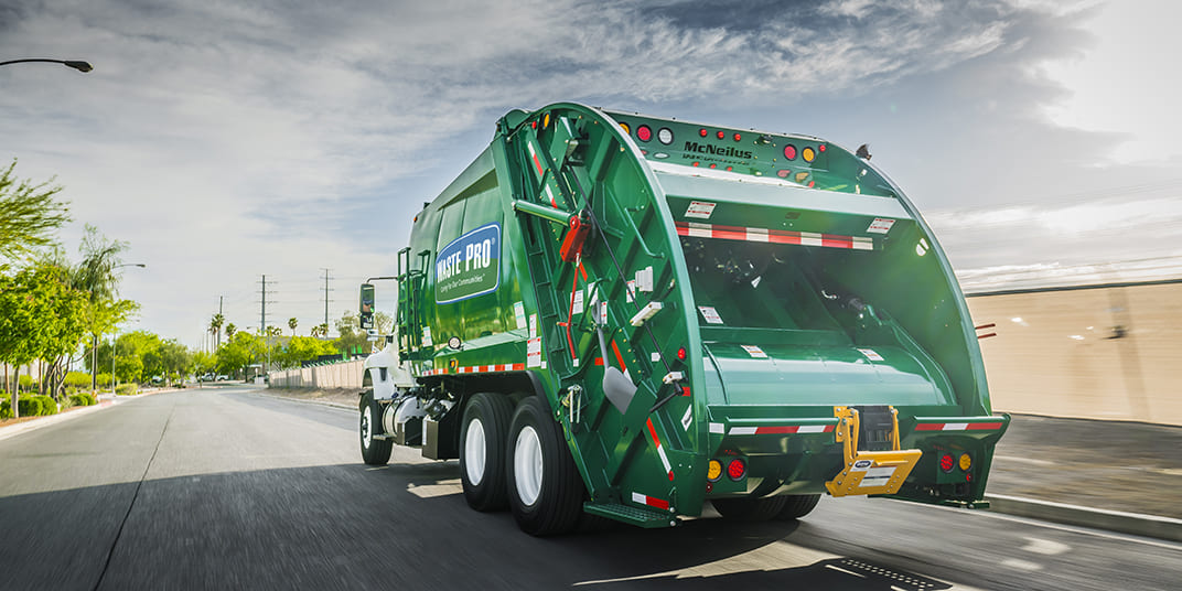 Green rear loader refuse collection vehicle driving on a road