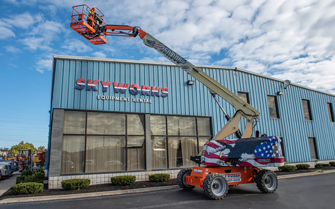 Red, white and blue 250,000th JLG boom lift positioned outside a blue Skyworks building