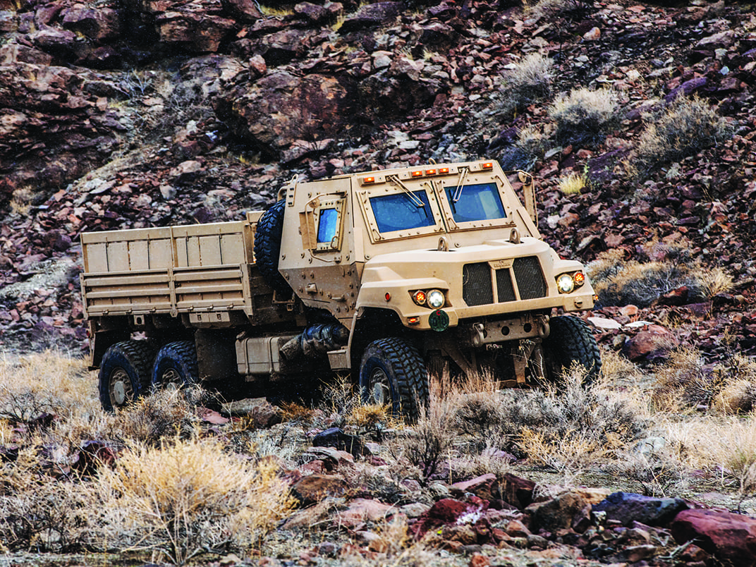 Khaki colored FMTV-A2 vehicle driving outside on rough terrain